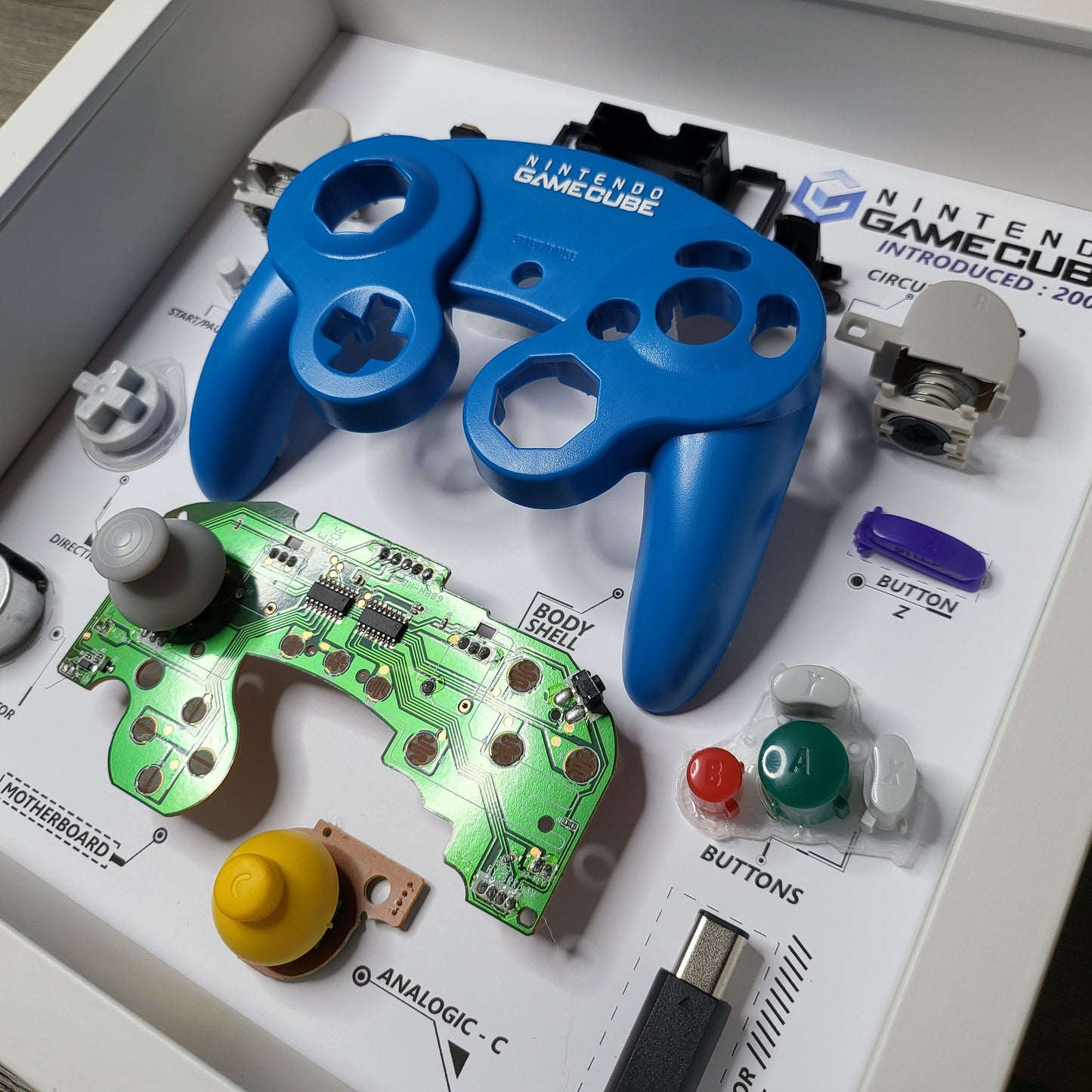 Shadow Box 10x10 with wood frame and polycarbonate glass for wall and Tabletop containing a disassembled controller for Playstation and Nintendo