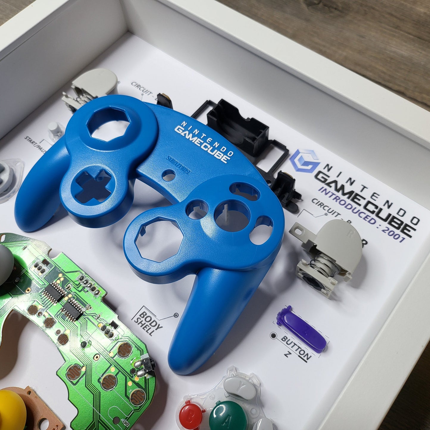 Shadow Box 10x10 with wood frame and polycarbonate glass for wall and Tabletop containing a disassembled controller for Playstation and Nintendo