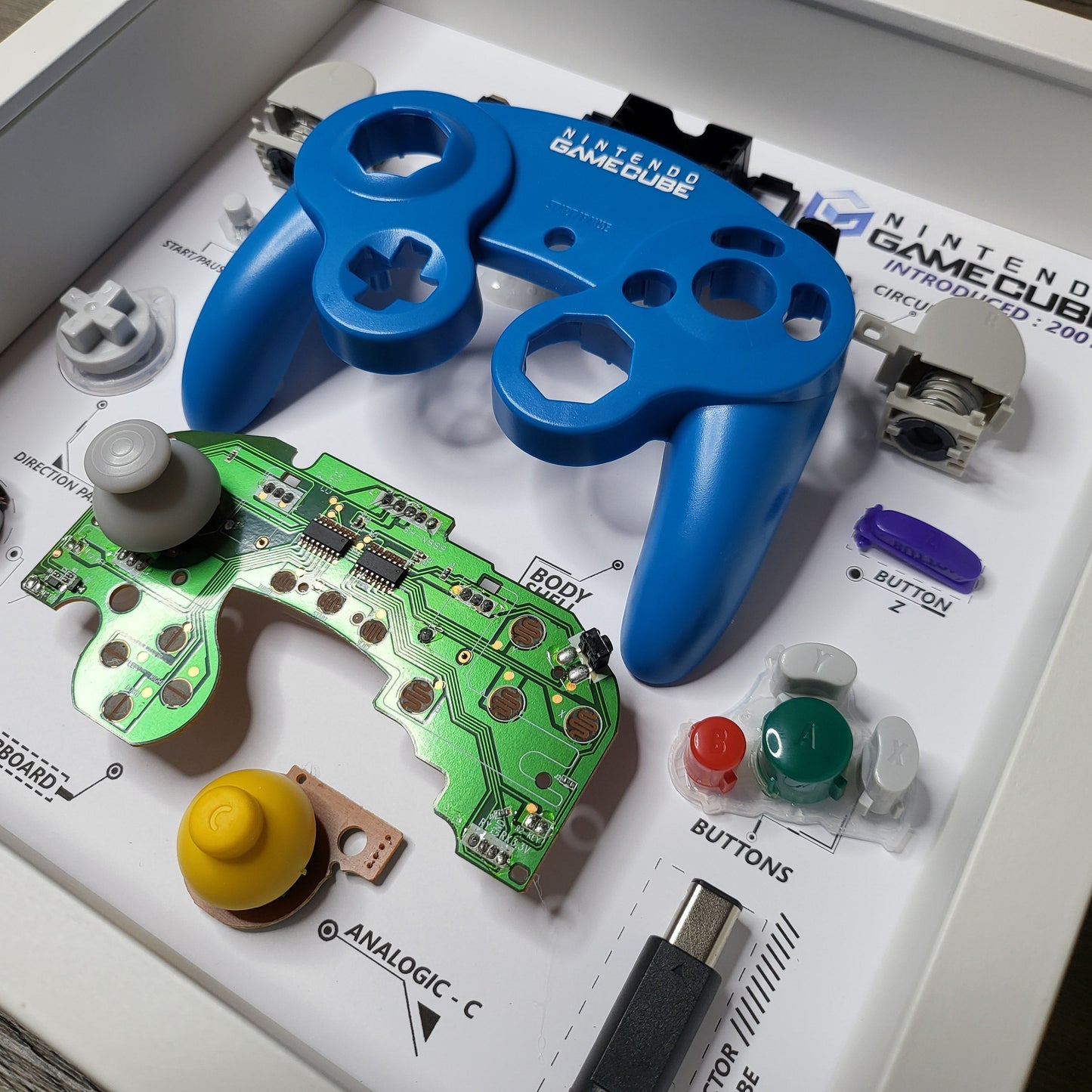 Shadow Box 10x10 with wood frame and polycarbonate glass for wall and Tabletop containing a disassembled controller for Playstation and Nintendo