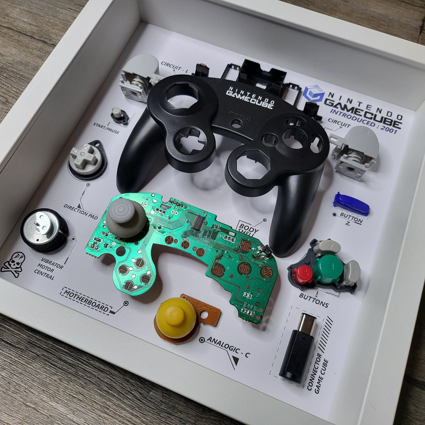 Shadow Box 10x10 with wood frame and polycarbonate glass for wall and Tabletop containing a disassembled controller for Playstation and Nintendo