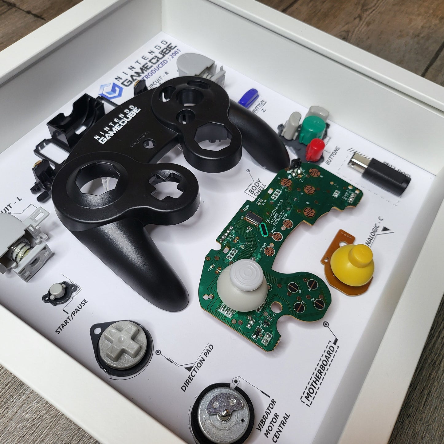 Shadow Box 10x10 with wood frame and polycarbonate glass for wall and Tabletop containing a disassembled controller for Playstation and Nintendo