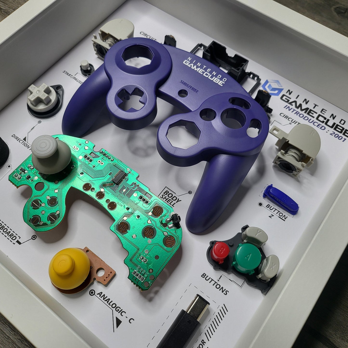 Shadow Box 10x10 with wood frame and polycarbonate glass for wall and Tabletop containing a disassembled controller for Playstation and Nintendo
