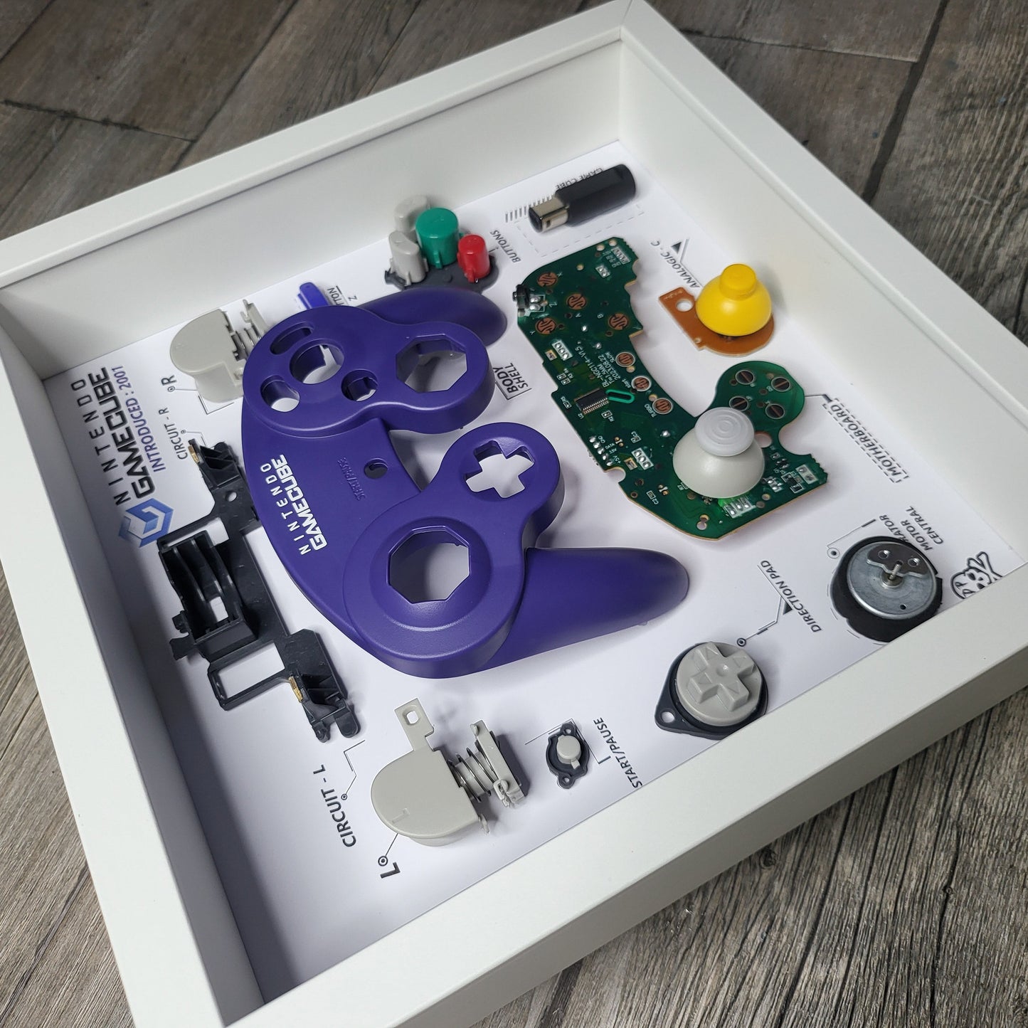 Shadow Box 10x10 with wood frame and polycarbonate glass for wall and Tabletop containing a disassembled controller for Playstation and Nintendo