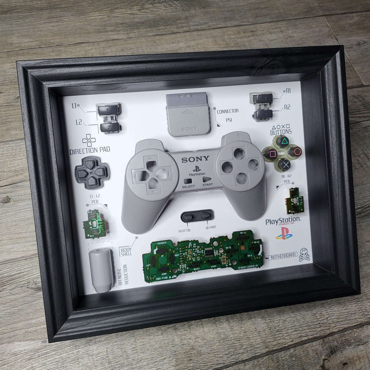 Shadow Box 10x10 with wood frame and polycarbonate glass for wall and Tabletop containing a disassembled controller for Playstation and Nintendo