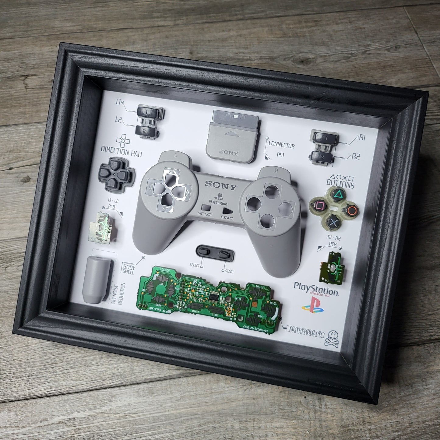 Shadow Box 10x10 with wood frame and polycarbonate glass for wall and Tabletop containing a disassembled controller for Playstation and Nintendo