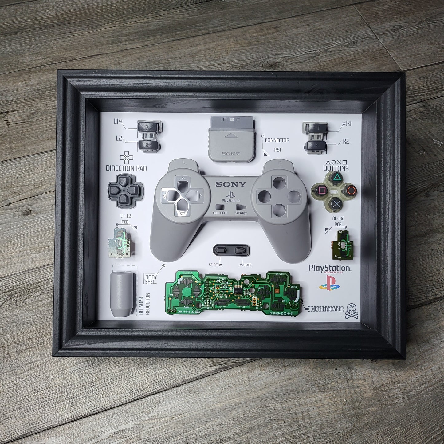 Shadow Box 10x10 with wood frame and polycarbonate glass for wall and Tabletop containing a disassembled controller for Playstation and Nintendo