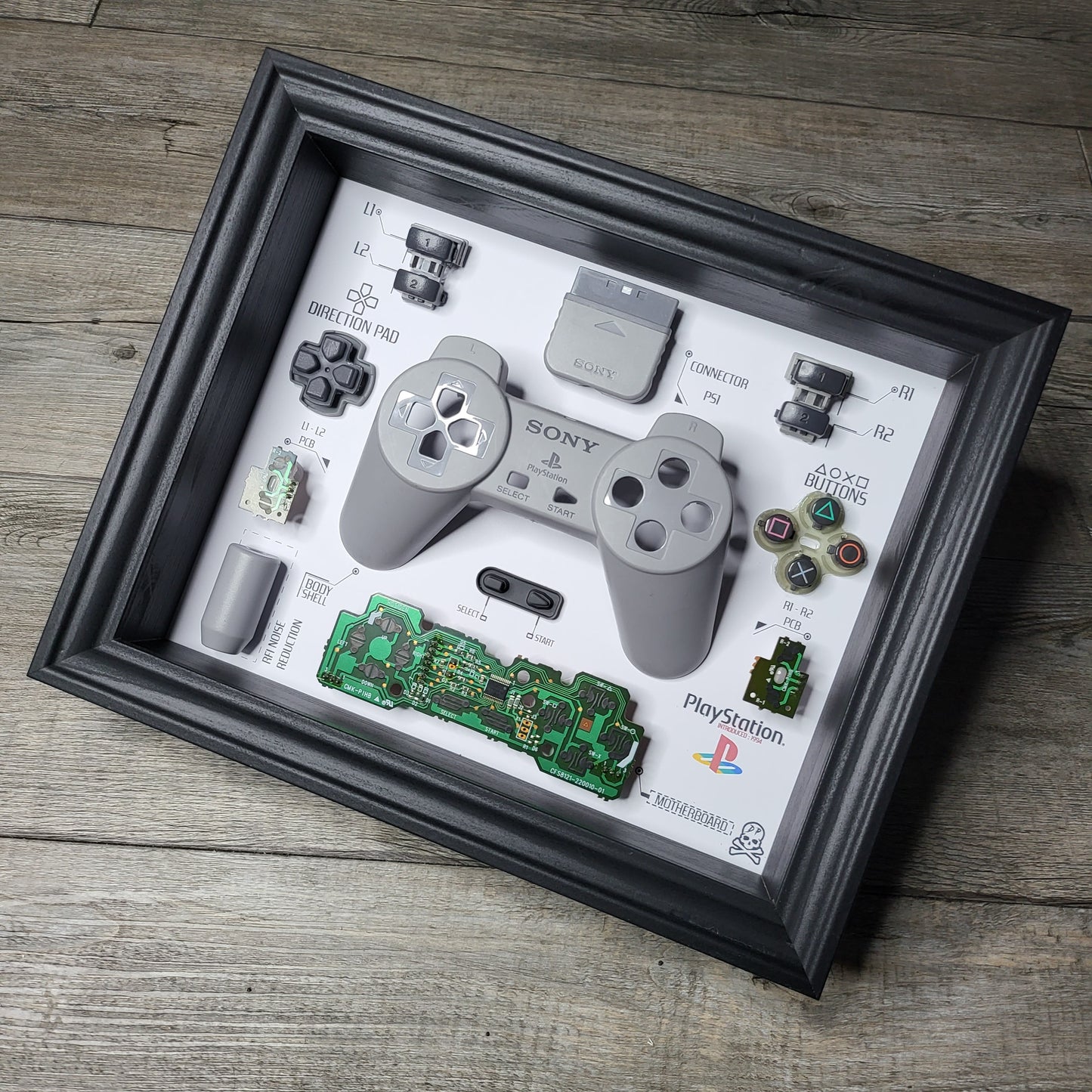 Shadow Box 10x10 with wood frame and polycarbonate glass for wall and Tabletop containing a disassembled controller for Playstation and Nintendo