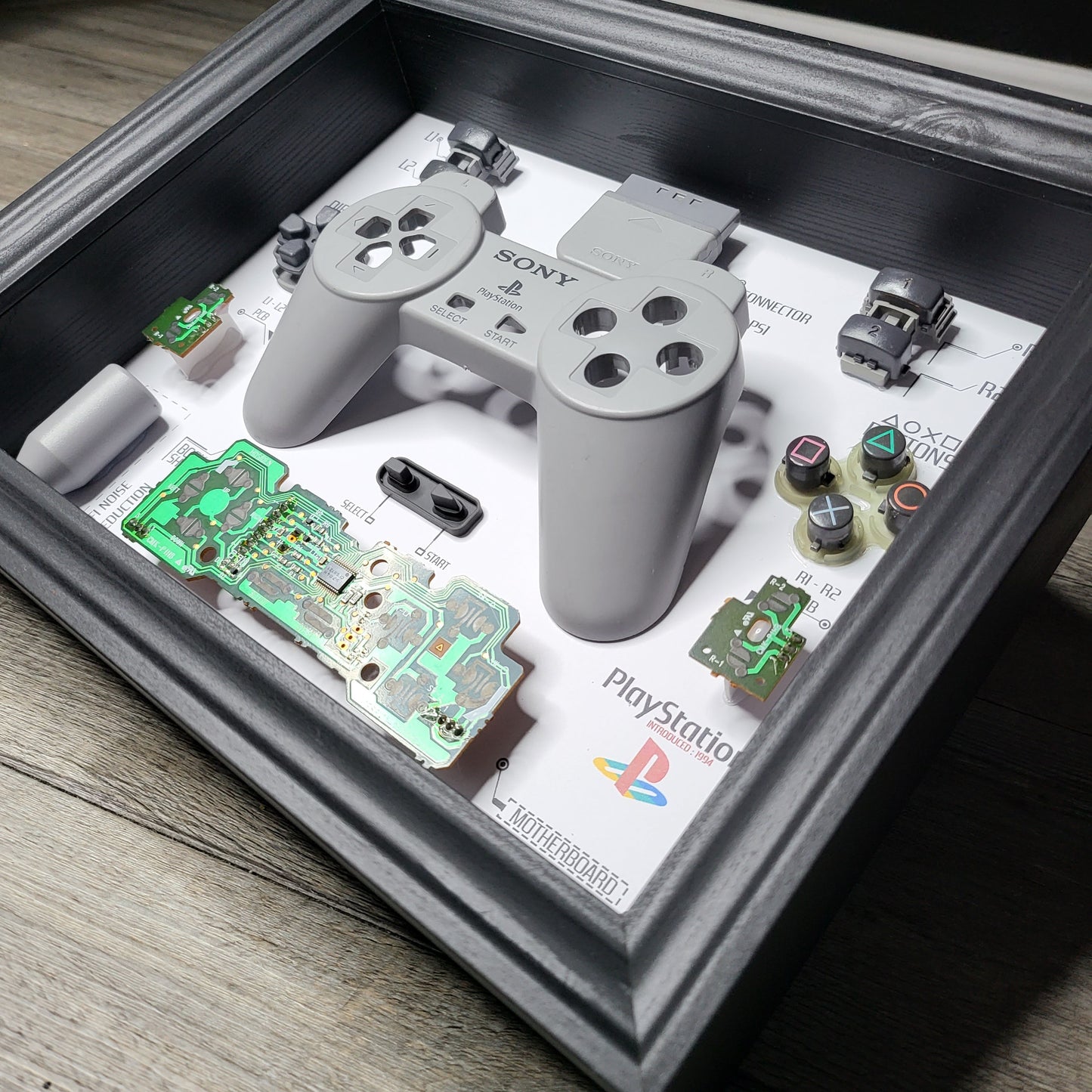 Shadow Box 10x10 with wood frame and polycarbonate glass for wall and Tabletop containing a disassembled controller for Playstation and Nintendo
