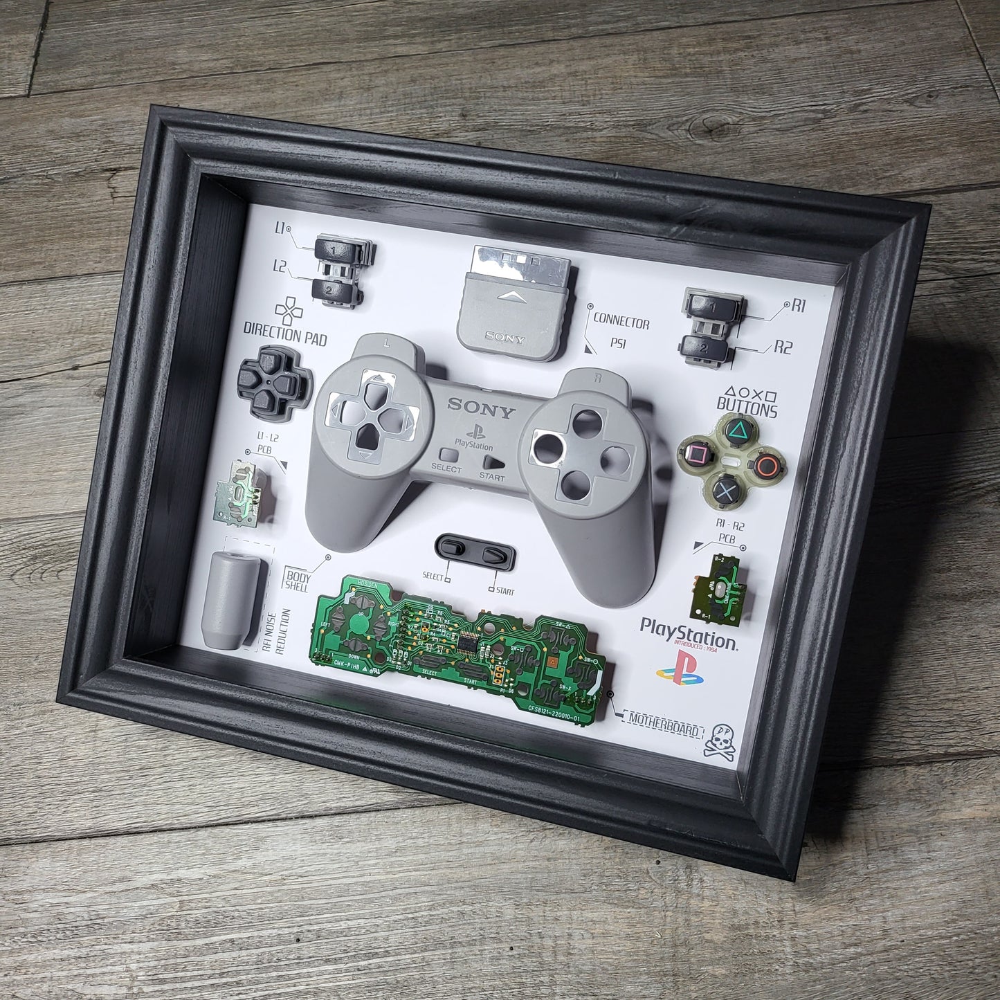 Shadow Box 10x10 with wood frame and polycarbonate glass for wall and Tabletop containing a disassembled controller for Playstation and Nintendo