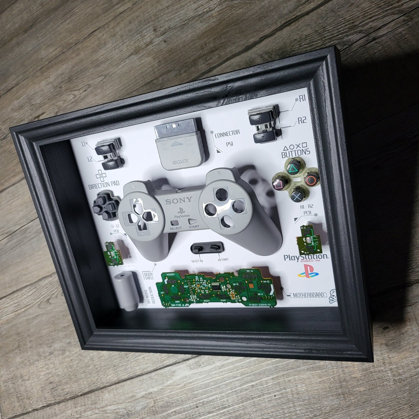 Shadow Box 10x10 with wood frame and polycarbonate glass for wall and Tabletop containing a disassembled controller for Playstation and Nintendo