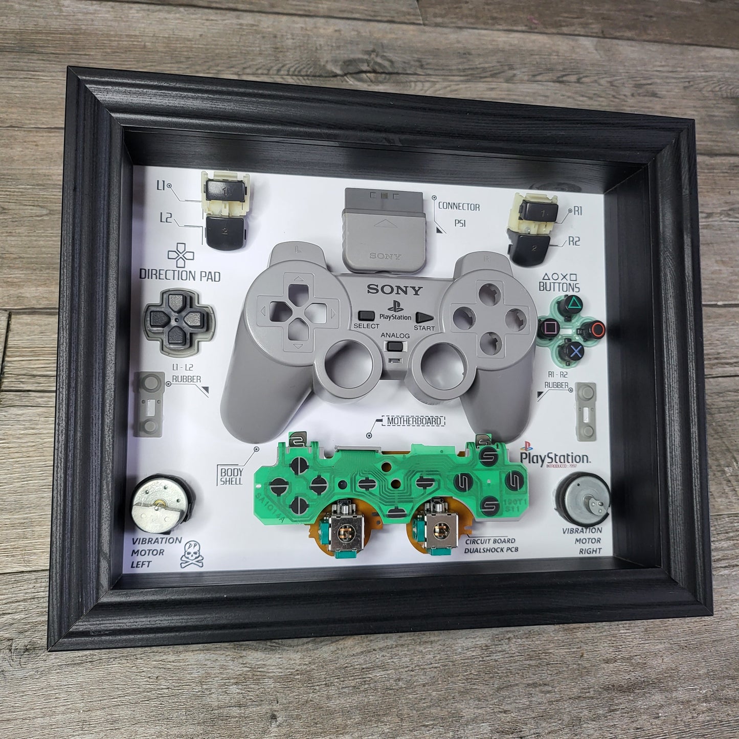 Shadow Box 10x10 with wood frame and polycarbonate glass for wall and Tabletop containing a disassembled controller for Playstation and Nintendo