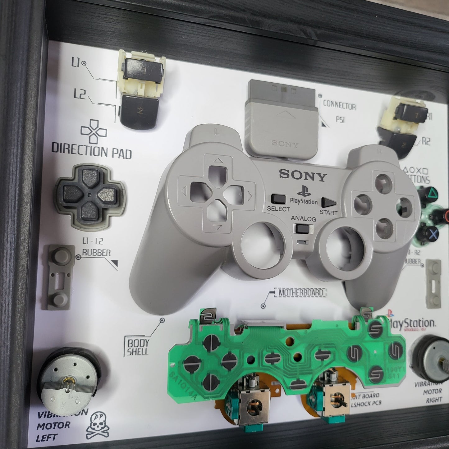 Shadow Box 10x10 with wood frame and polycarbonate glass for wall and Tabletop containing a disassembled controller for Playstation and Nintendo