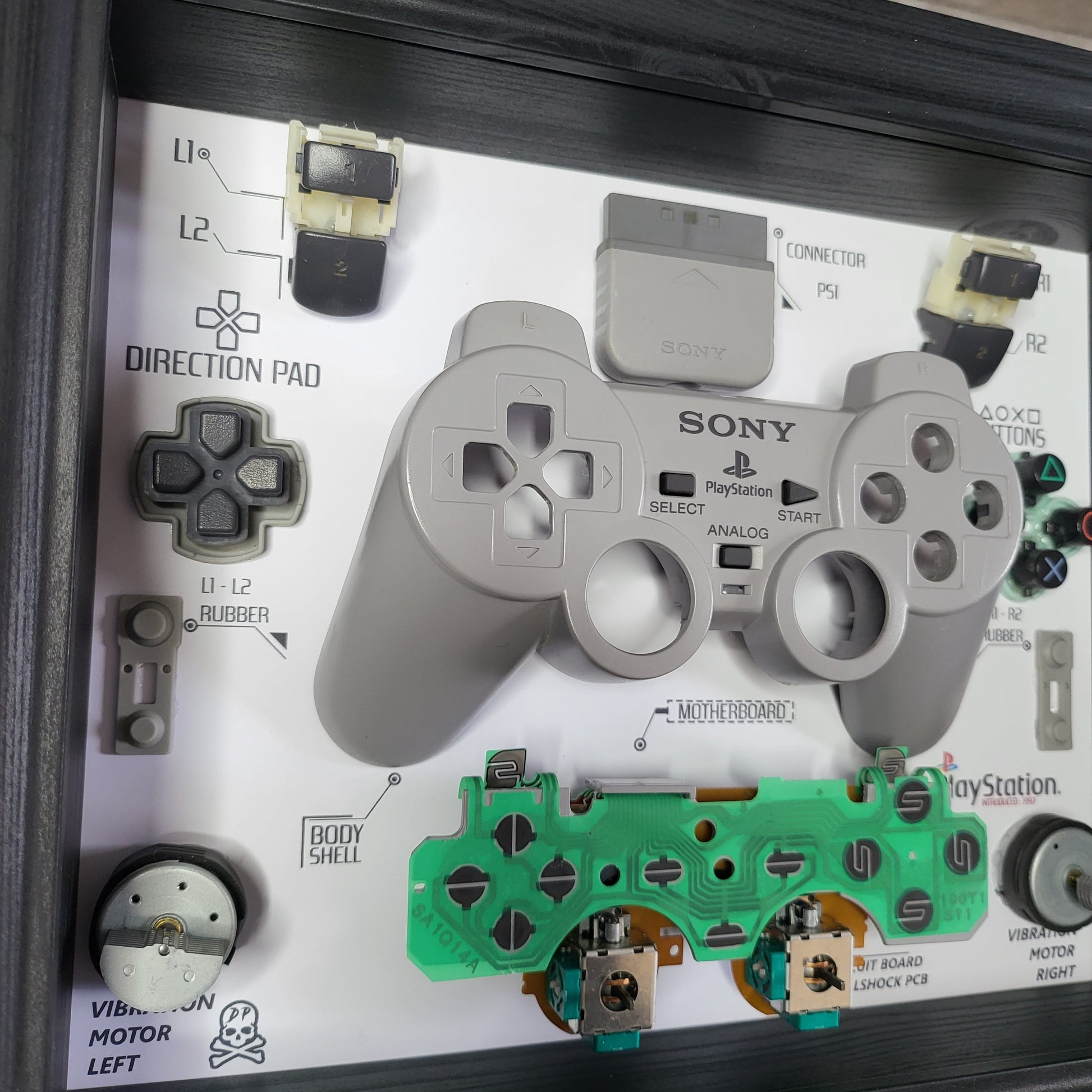 Shadow Box 10x10 with wood frame and polycarbonate glass for wall and Tabletop containing a disassembled controller for Playstation and Nintendo