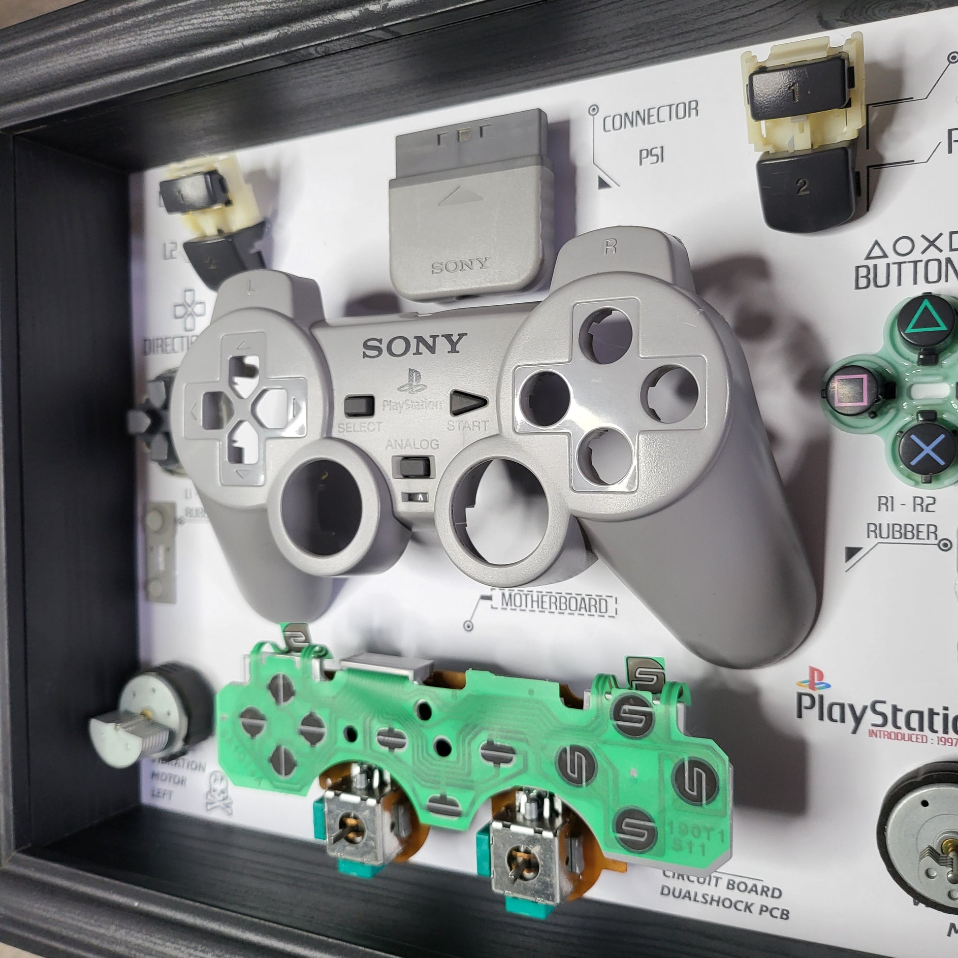 Shadow Box 10x10 with wood frame and polycarbonate glass for wall and Tabletop containing a disassembled controller for Playstation and Nintendo