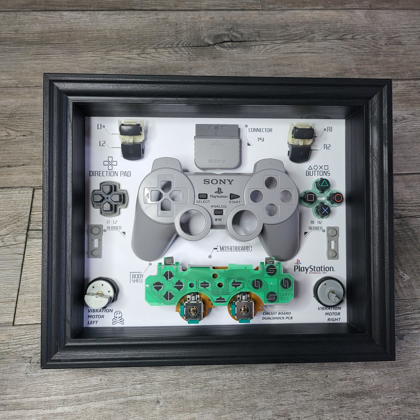 Shadow Box 10x10 with wood frame and polycarbonate glass for wall and Tabletop containing a disassembled controller for Playstation and Nintendo