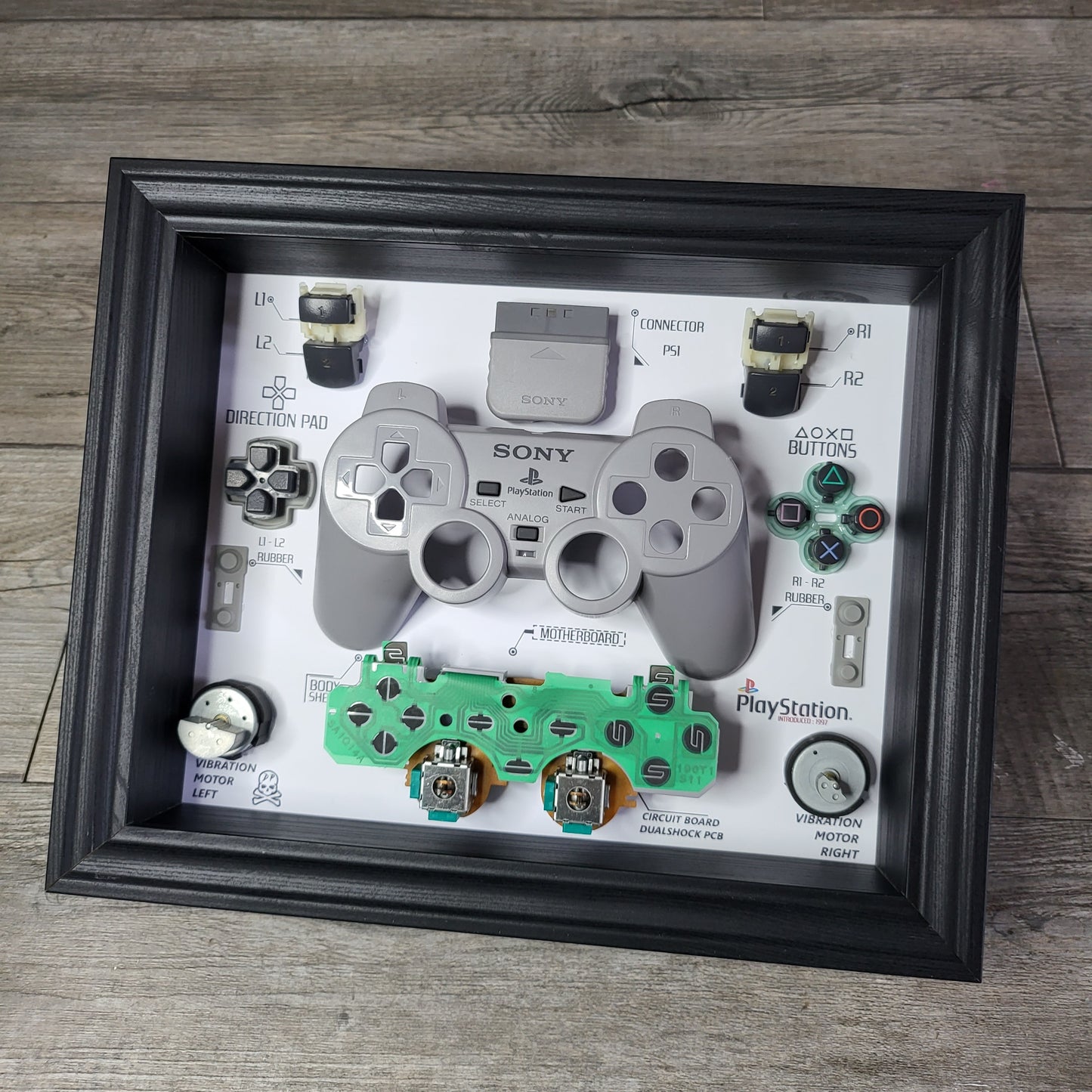Shadow Box 10x10 with wood frame and polycarbonate glass for wall and Tabletop containing a disassembled controller for Playstation and Nintendo