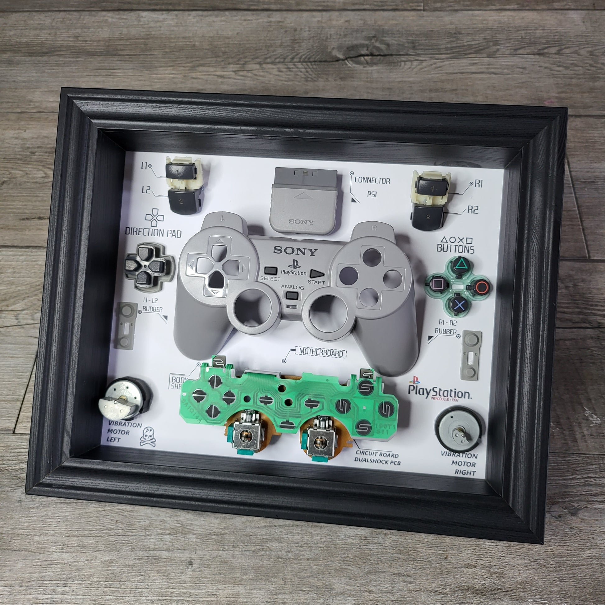 Shadow Box 10x10 with wood frame and polycarbonate glass for wall and Tabletop containing a disassembled controller for Playstation and Nintendo