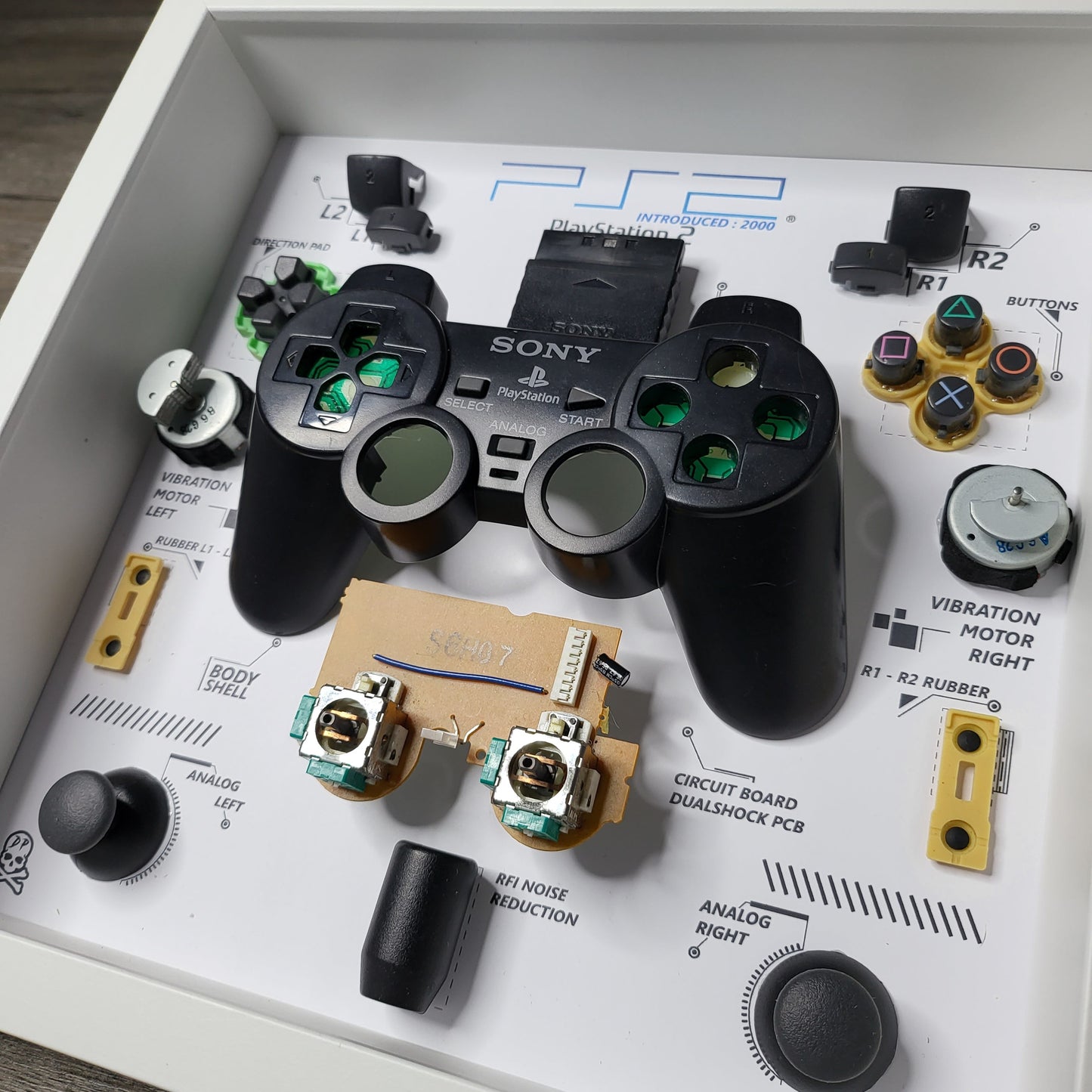 Shadow Box 10x10 with wood frame and polycarbonate glass for wall and Tabletop containing a disassembled controller for Playstation and Nintendo