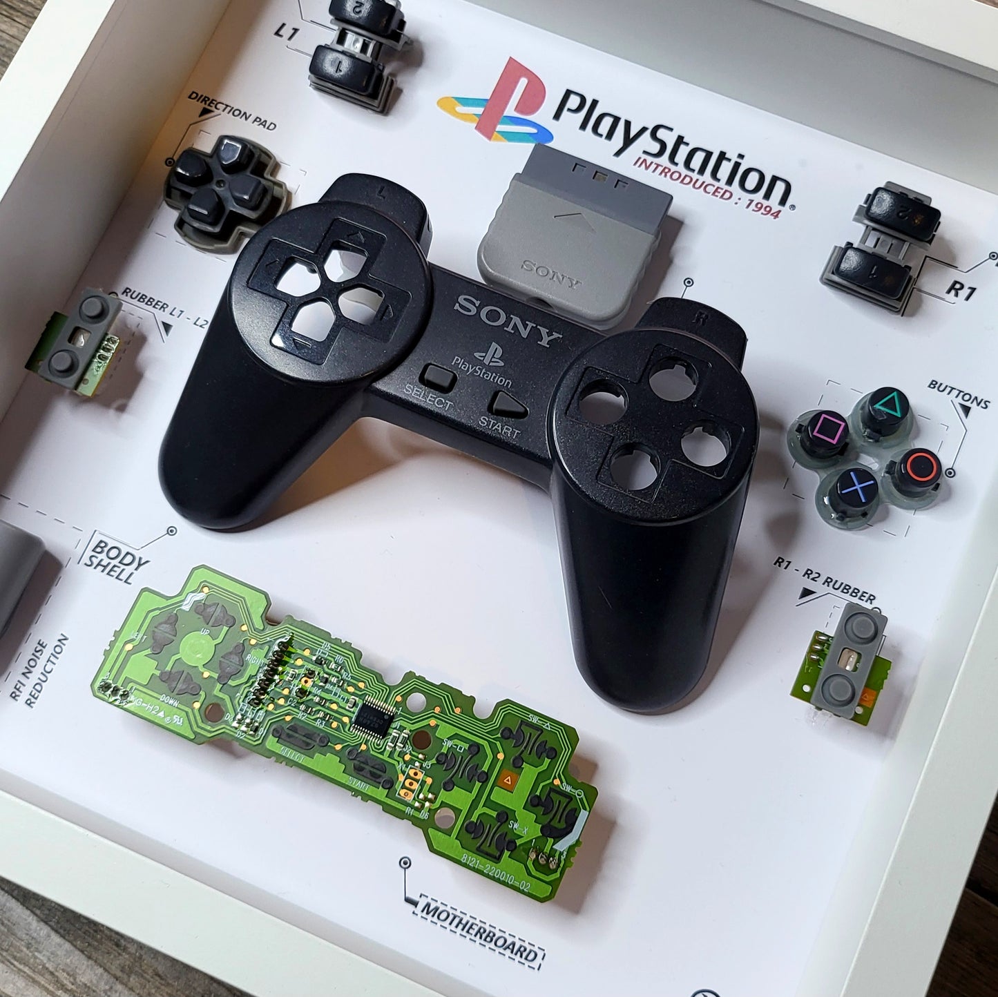 Shadow Box 10x10 with wood frame and polycarbonate glass for wall and Tabletop containing a disassembled controller for Playstation and Nintendo