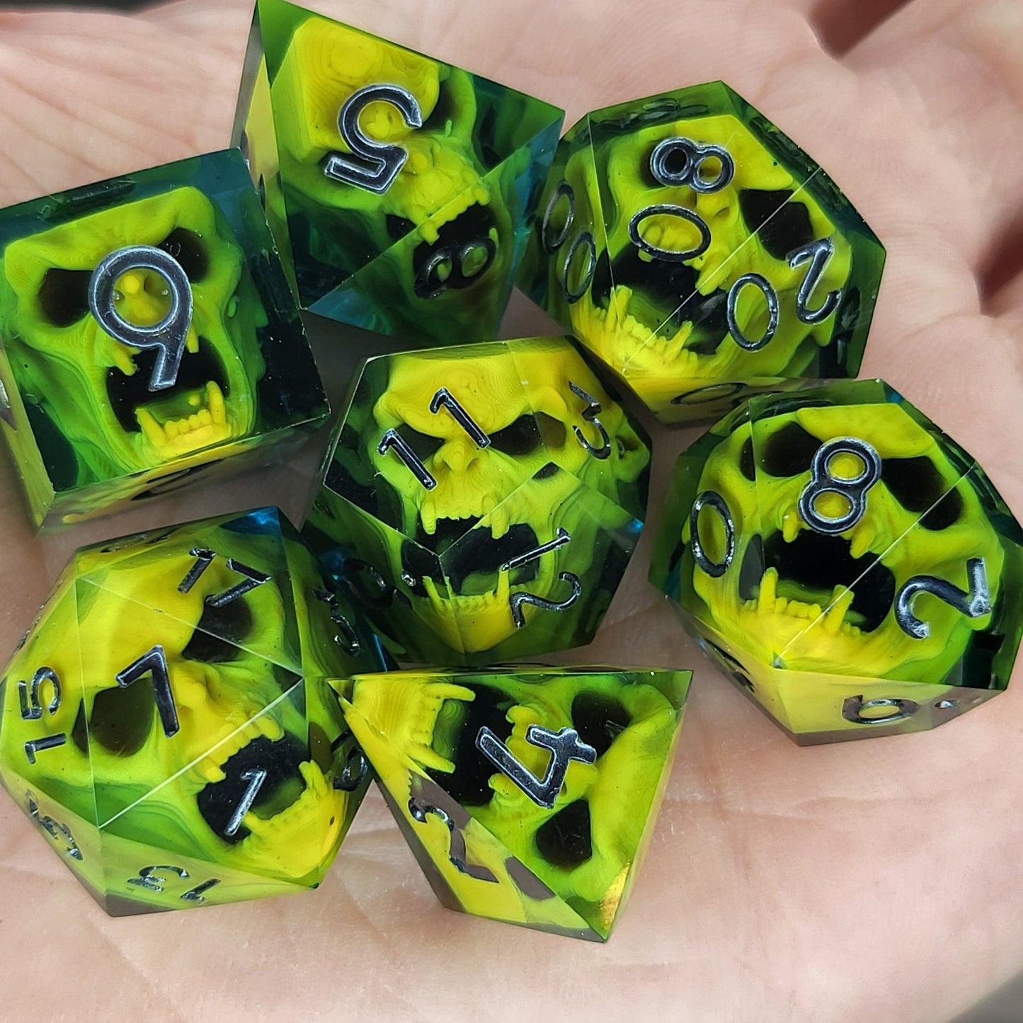 Blue resin DnD dice set with bright yellow skulls inside and silver engraved numbers