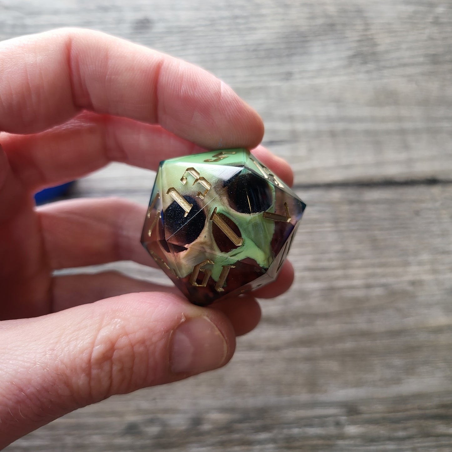 A single D20 resin die with a pale yellow skull inside, red resin and golden numbers for DND Dungeons and Dragons and role playing games RPG