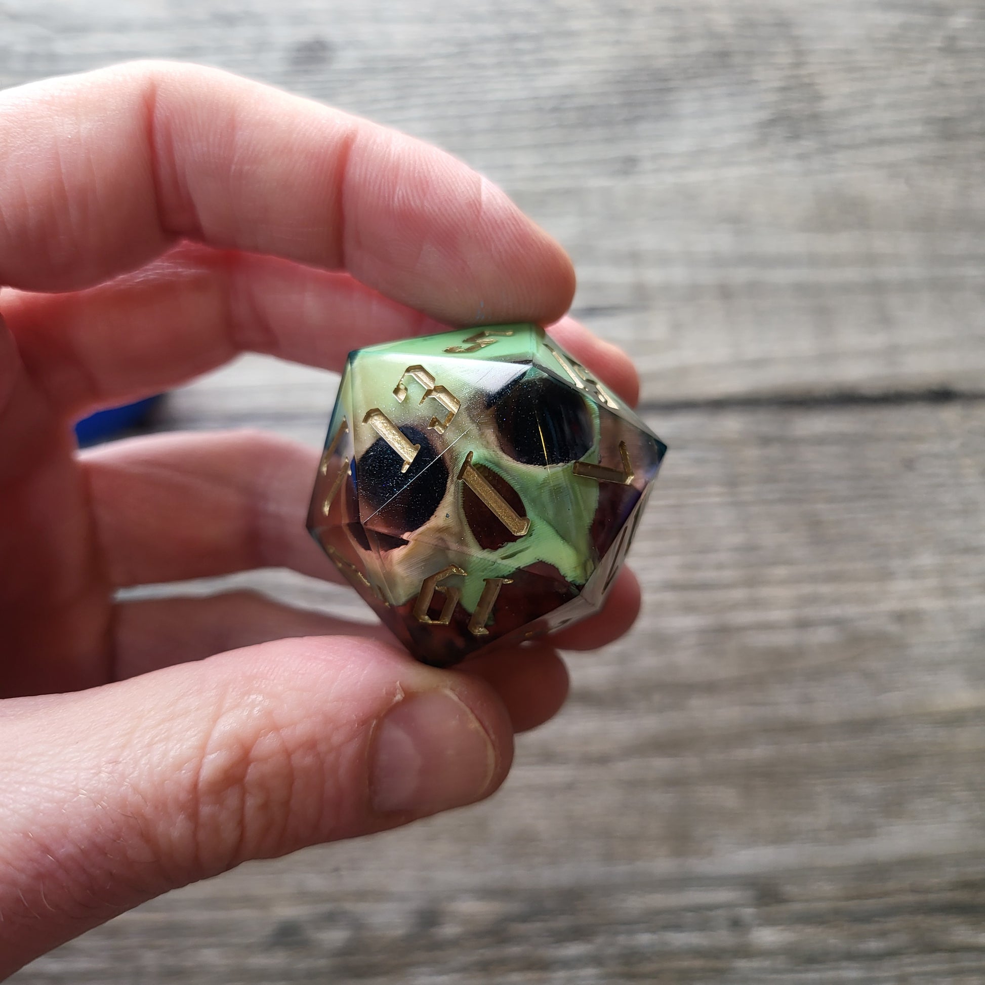 A single D20 resin die with a pale yellow skull inside, red resin and golden numbers for DND Dungeons and Dragons and role playing games RPG