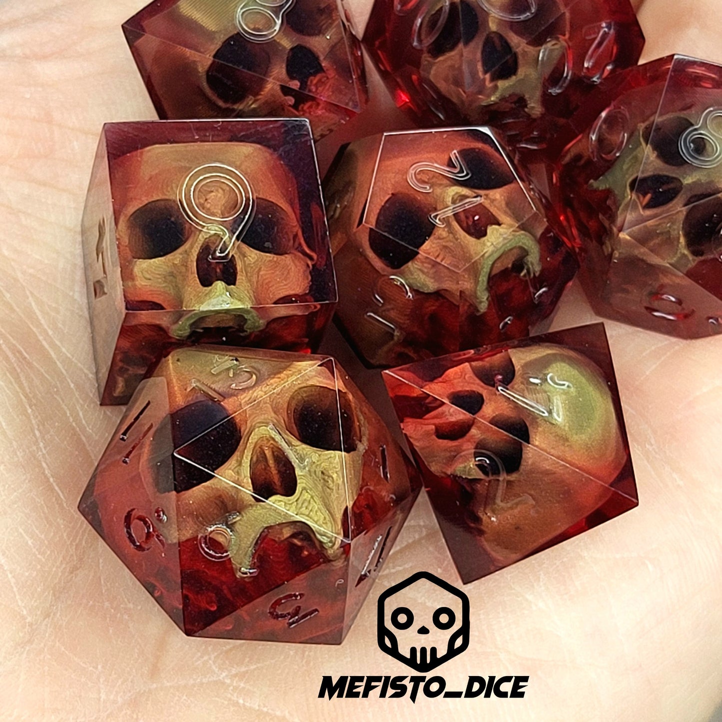 Handmade translucent red resin dice set with embedded skull designs resting in a hand. Gothic RPG polyhedral dice for Dungeons & Dragons and tabletop gaming with dark fantasy aesthetic