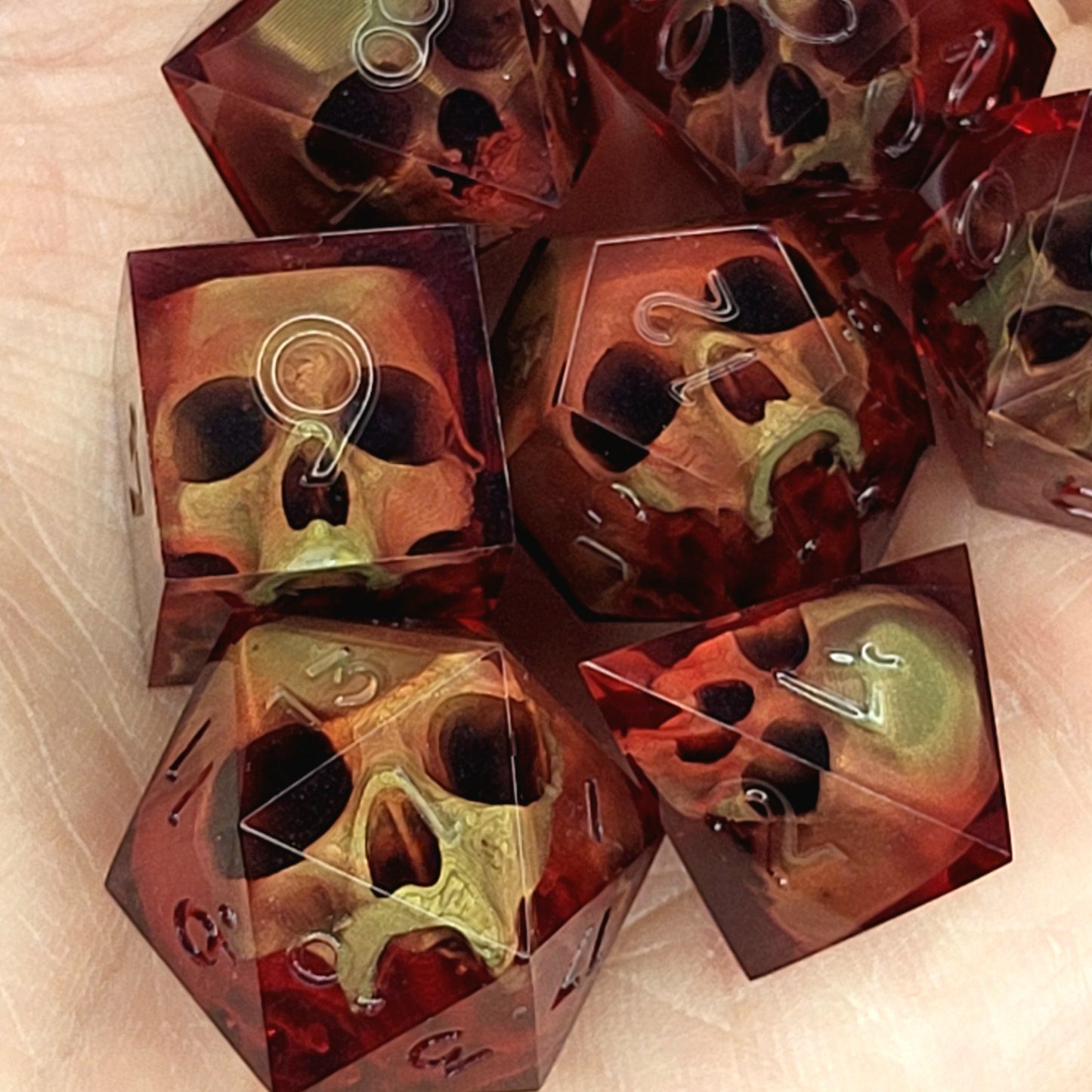 Handmade translucent red resin dice set with embedded skull designs resting in a hand. Gothic RPG polyhedral dice for Dungeons & Dragons and tabletop gaming with dark fantasy aesthetic