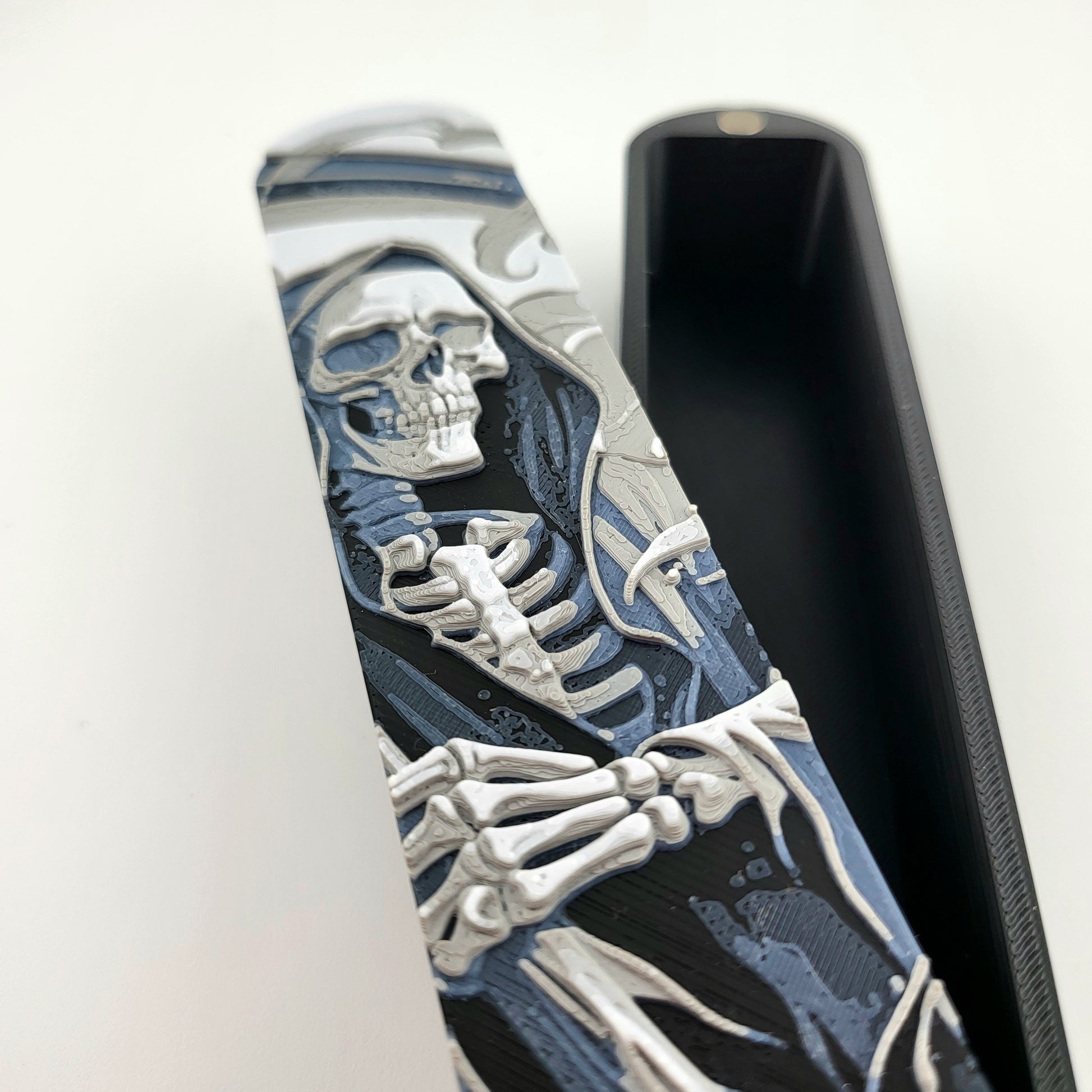 Close-up of a dice box featuring a detailed skeleton reaper illustration in shades of grey and blue, designed for storing RPG dice, handcrafted by Mefisto_Dice.