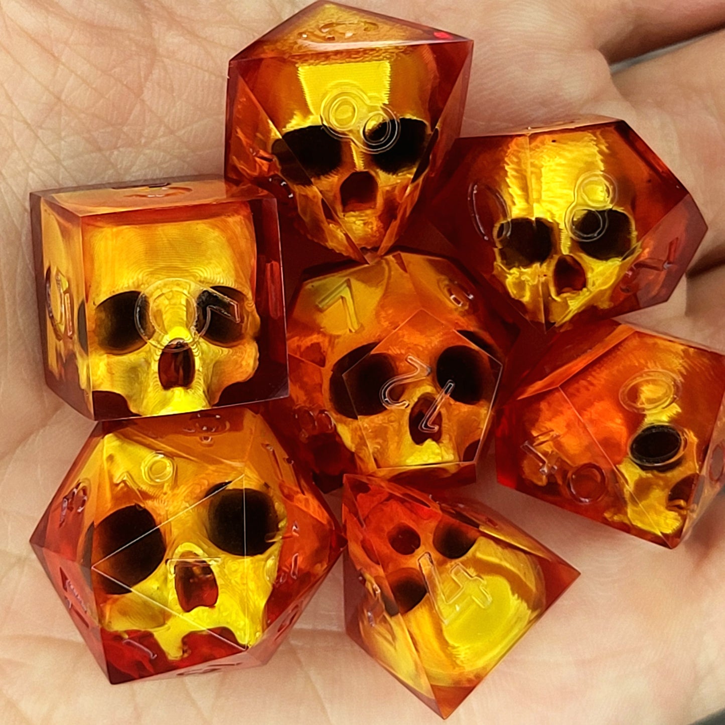 Handmade translucent red resin dice set with embedded skull designs resting in a hand. Gothic RPG polyhedral dice for Dungeons & Dragons and tabletop gaming with dark fantasy aesthetic