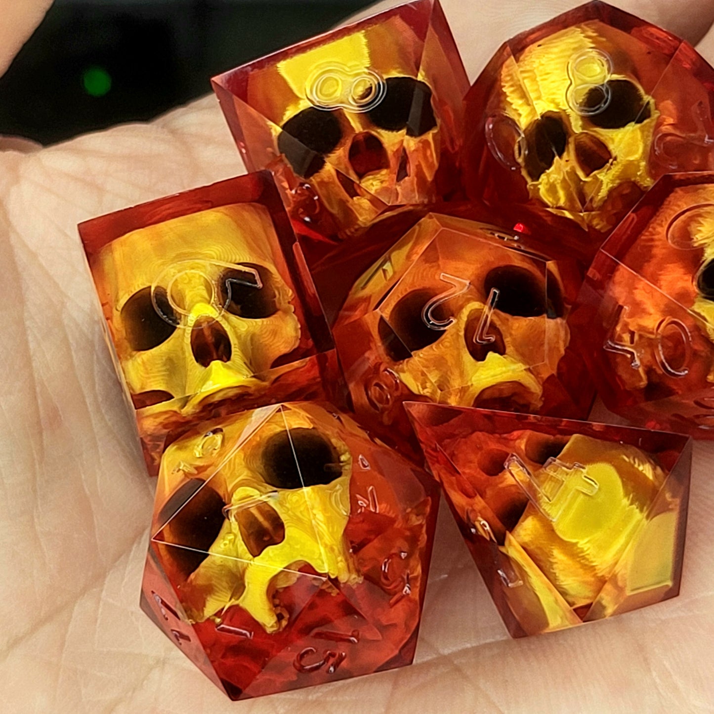 Handmade translucent red resin dice set with embedded skull designs resting in a hand. Gothic RPG polyhedral dice for Dungeons & Dragons and tabletop gaming with dark fantasy aesthetic