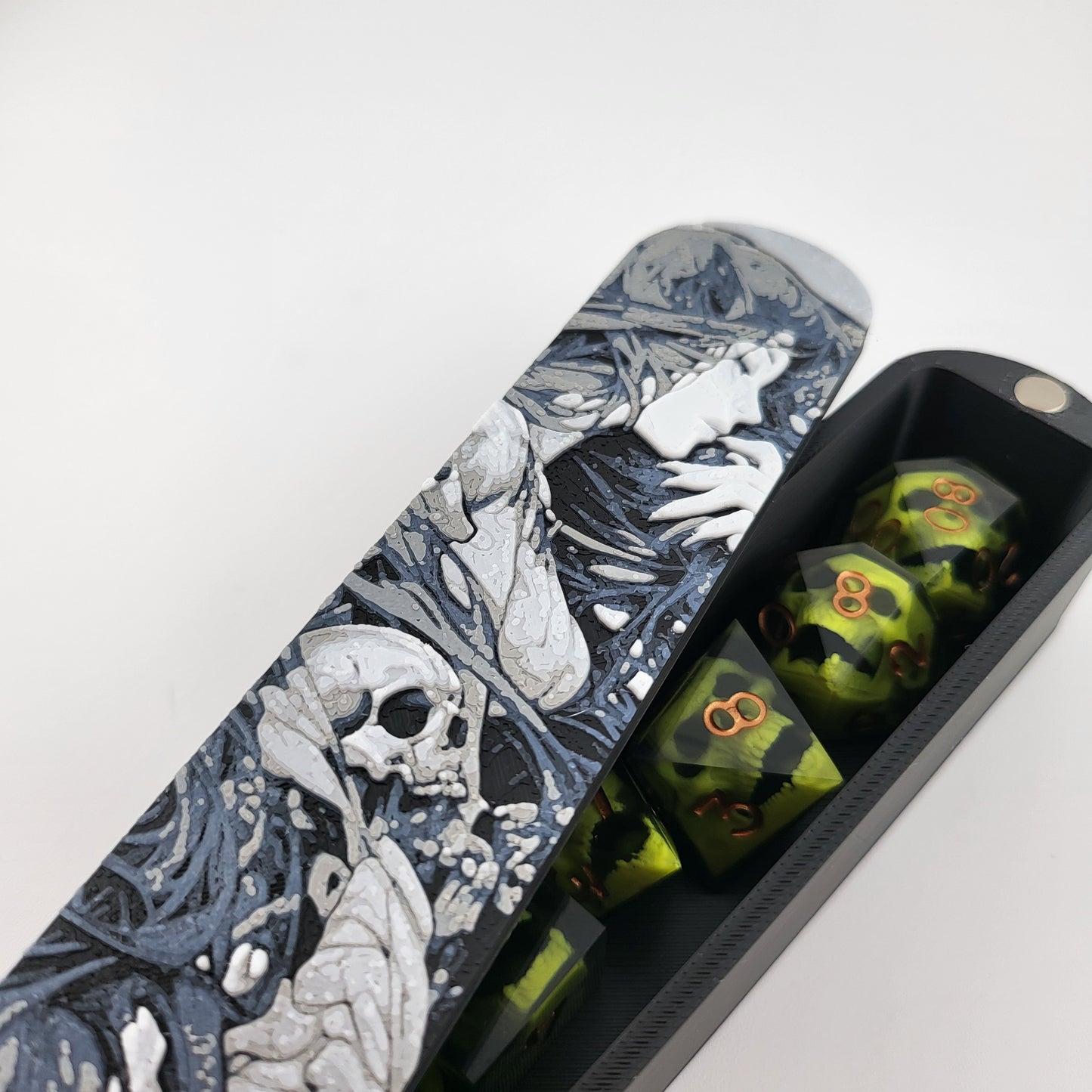 Close-up of a dice box featuring a detailed dark fantasy illustration of a woman surrounded by swirling shadows and skull motifs, shown partially open with RPG dice stored inside, designed by Mefisto_Dice.