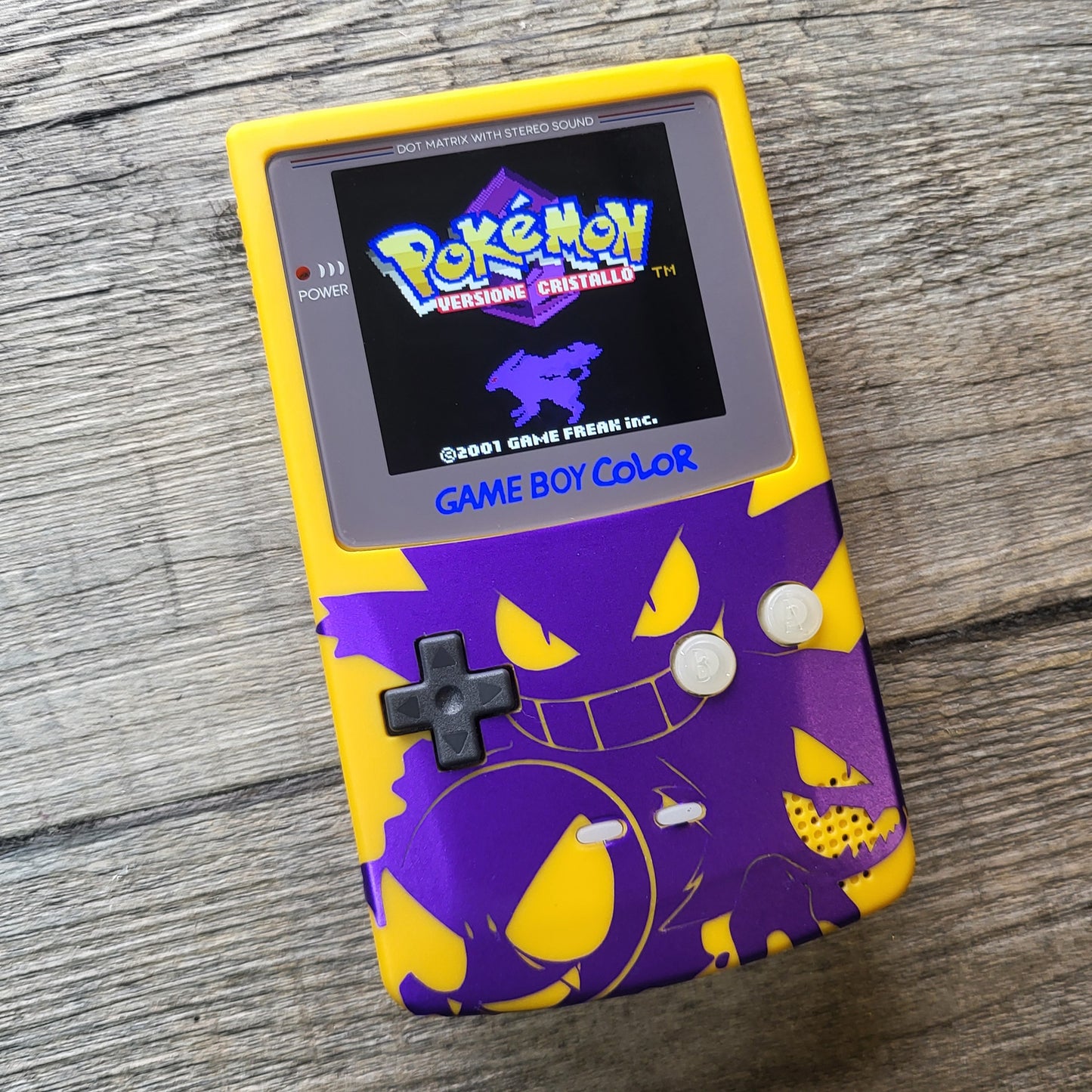 A customized Nintendo Gameboy color with yellow and purple Gengar pokemon on the front cover and backlit display