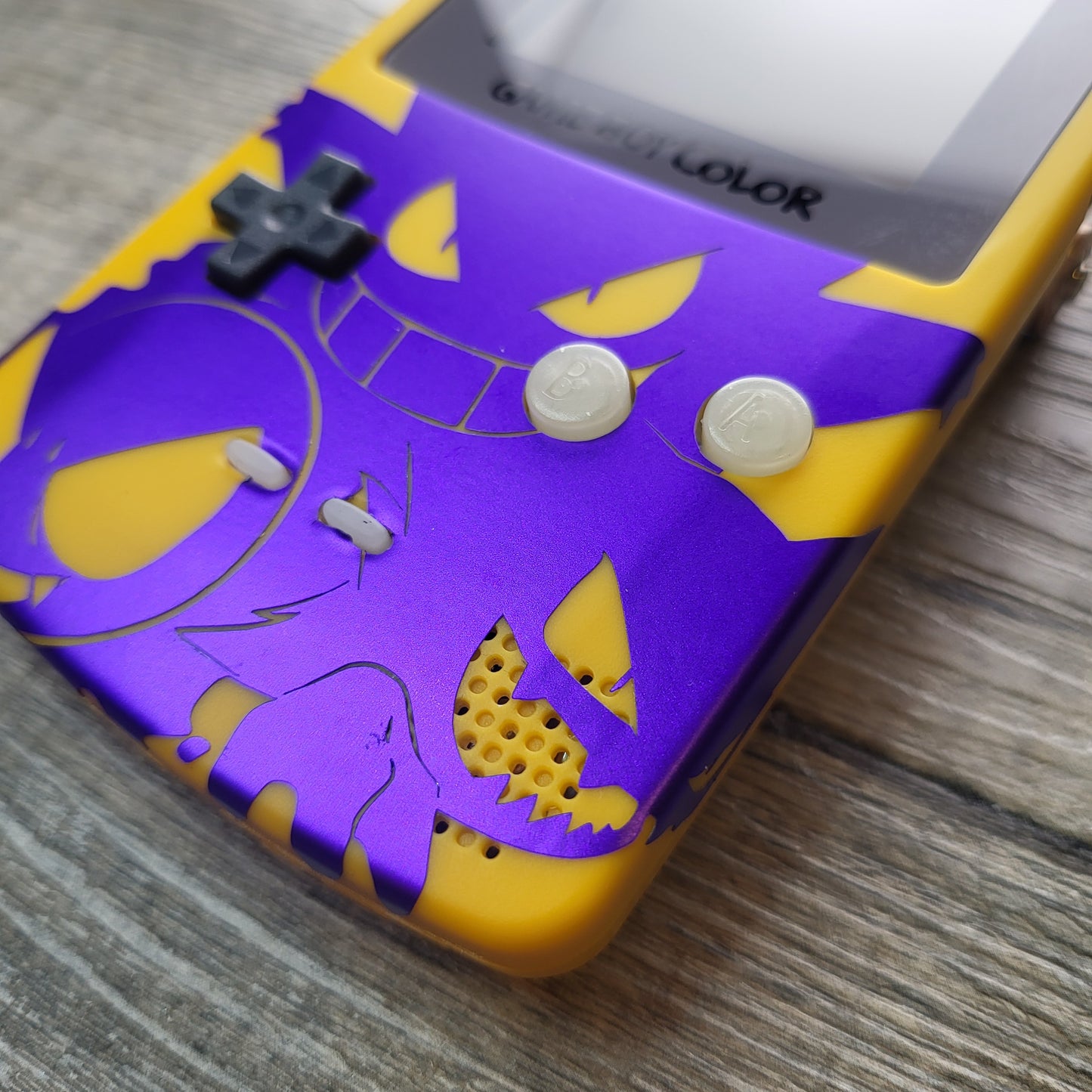 A customized Nintendo Gameboy color with yellow and purple Gengar pokemon on the front cover and backlit display