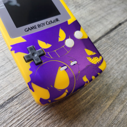 A customized Nintendo Gameboy color with yellow and purple Gengar pokemon on the front cover and backlit display