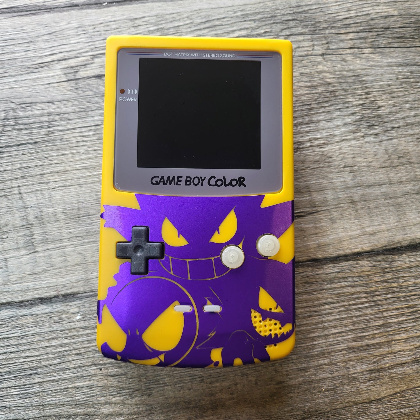 A customized Nintendo Gameboy color with yellow and purple Gengar pokemon on the front cover and backlit display