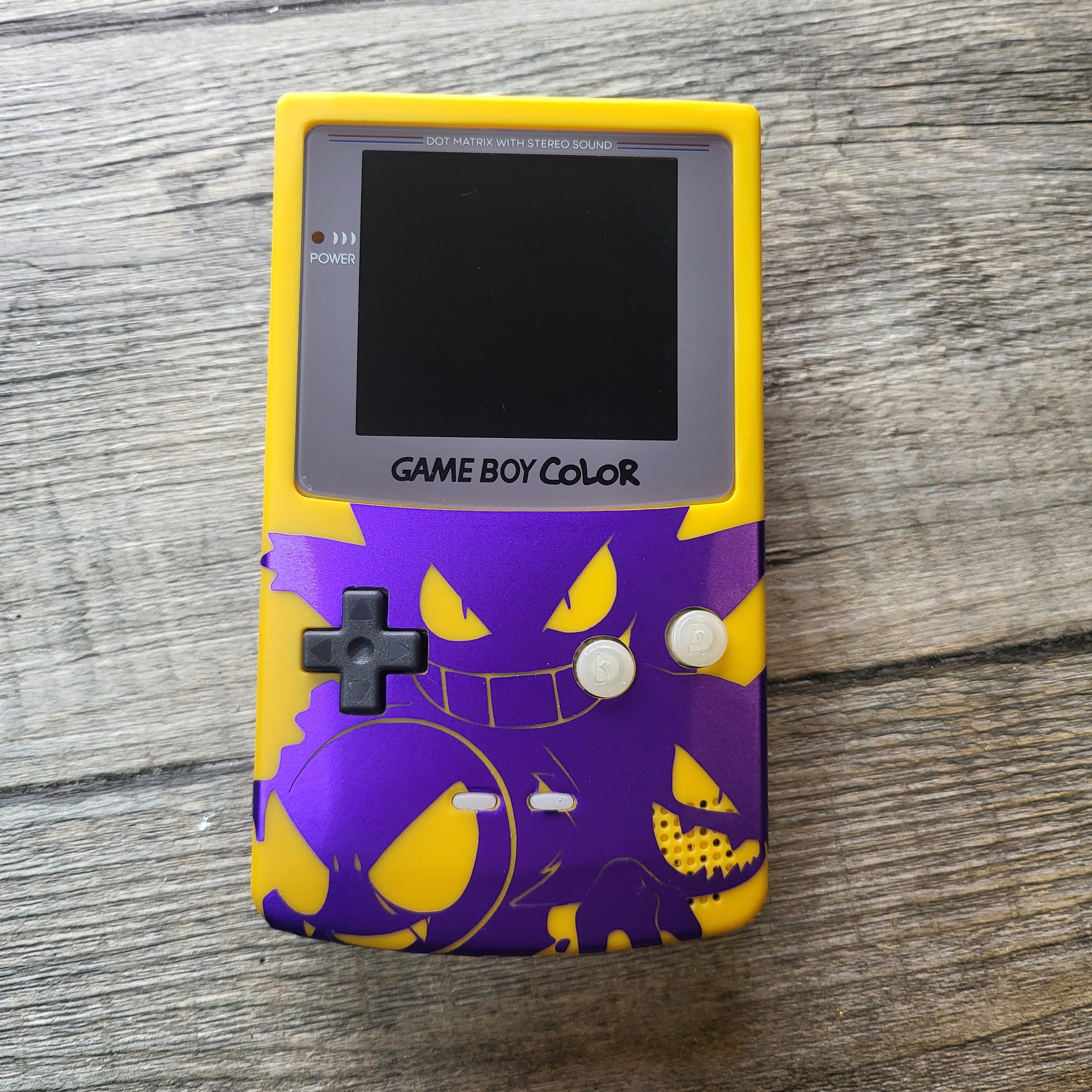 A customized Nintendo Gameboy color with yellow and purple Gengar pokemon on the front cover and backlit display