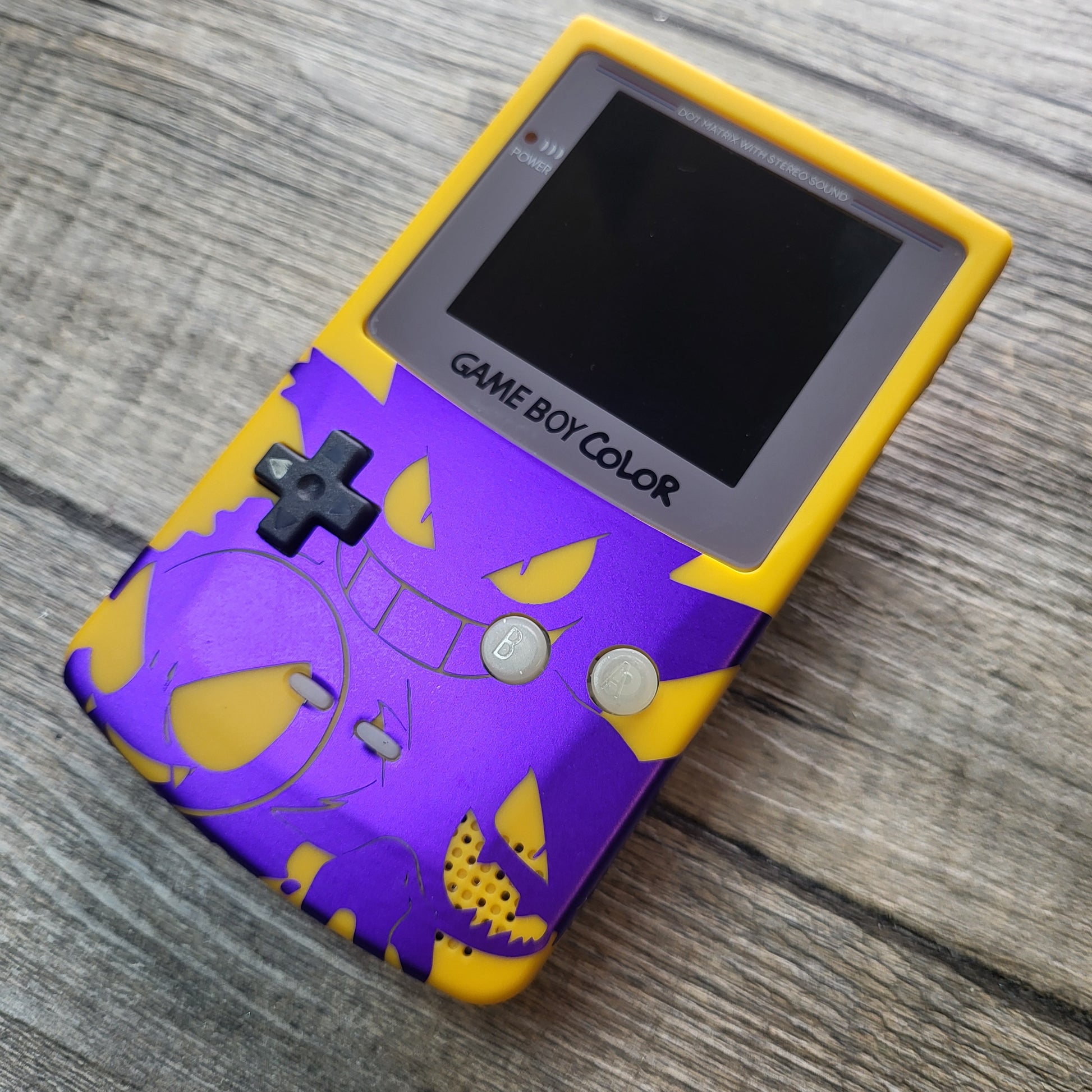 A customized Nintendo Gameboy color with yellow and purple Gengar pokemon on the front cover and backlit display