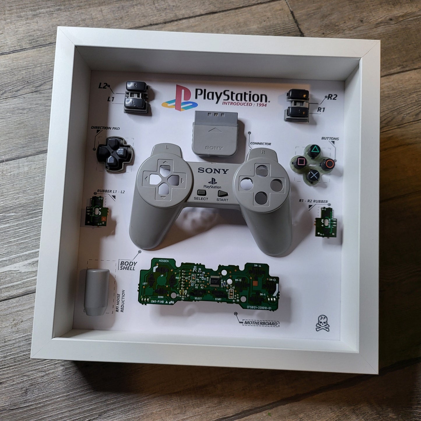 Shadow Box 10x10 with wood frame and polycarbonate glass for wall and Tabletop containing a disassembled controller for Playstation and Nintendo