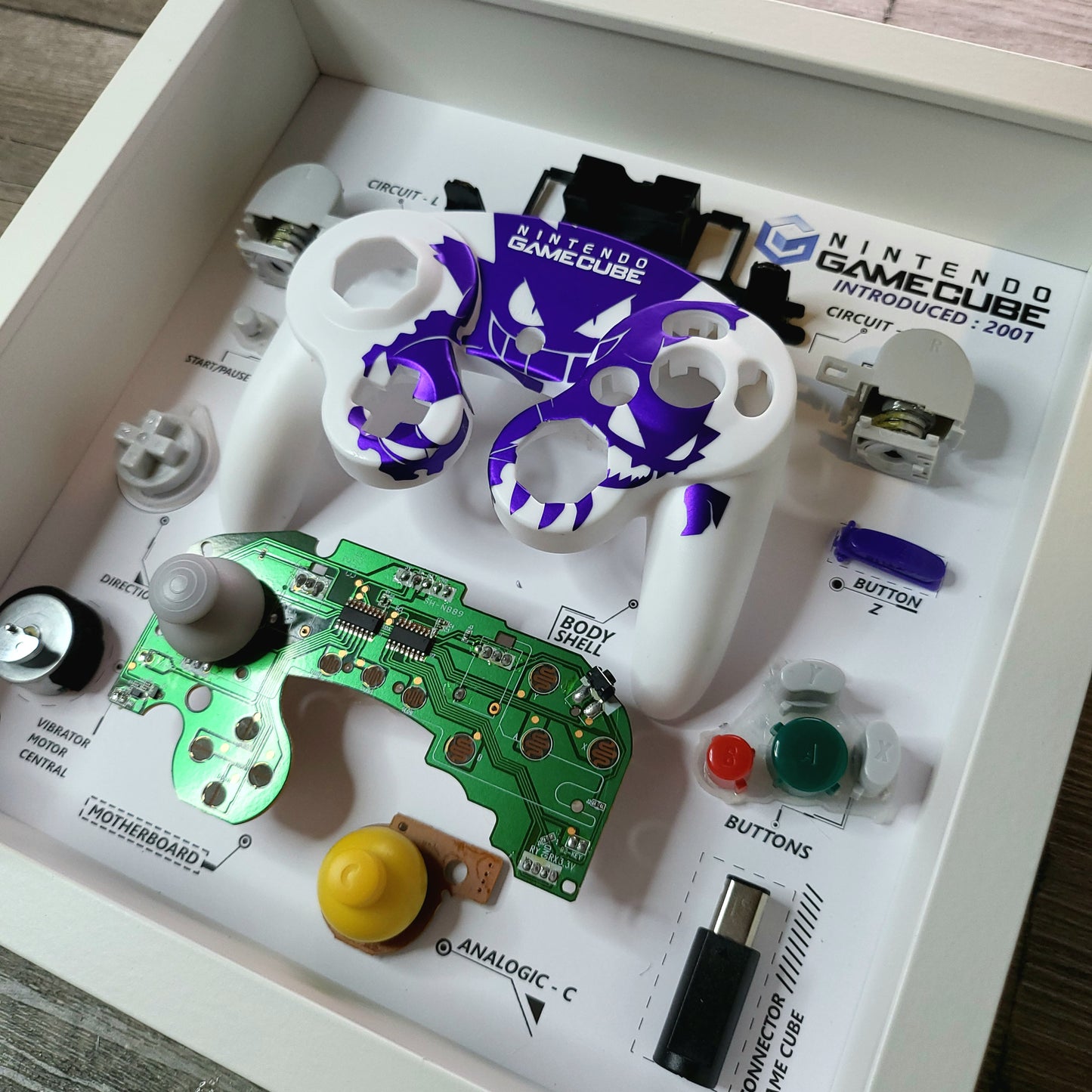 Shadow Box 10x10 with wood frame and polycarbonate glass for wall and Tabletop containing a disassembled controller for Playstation and Nintendo
