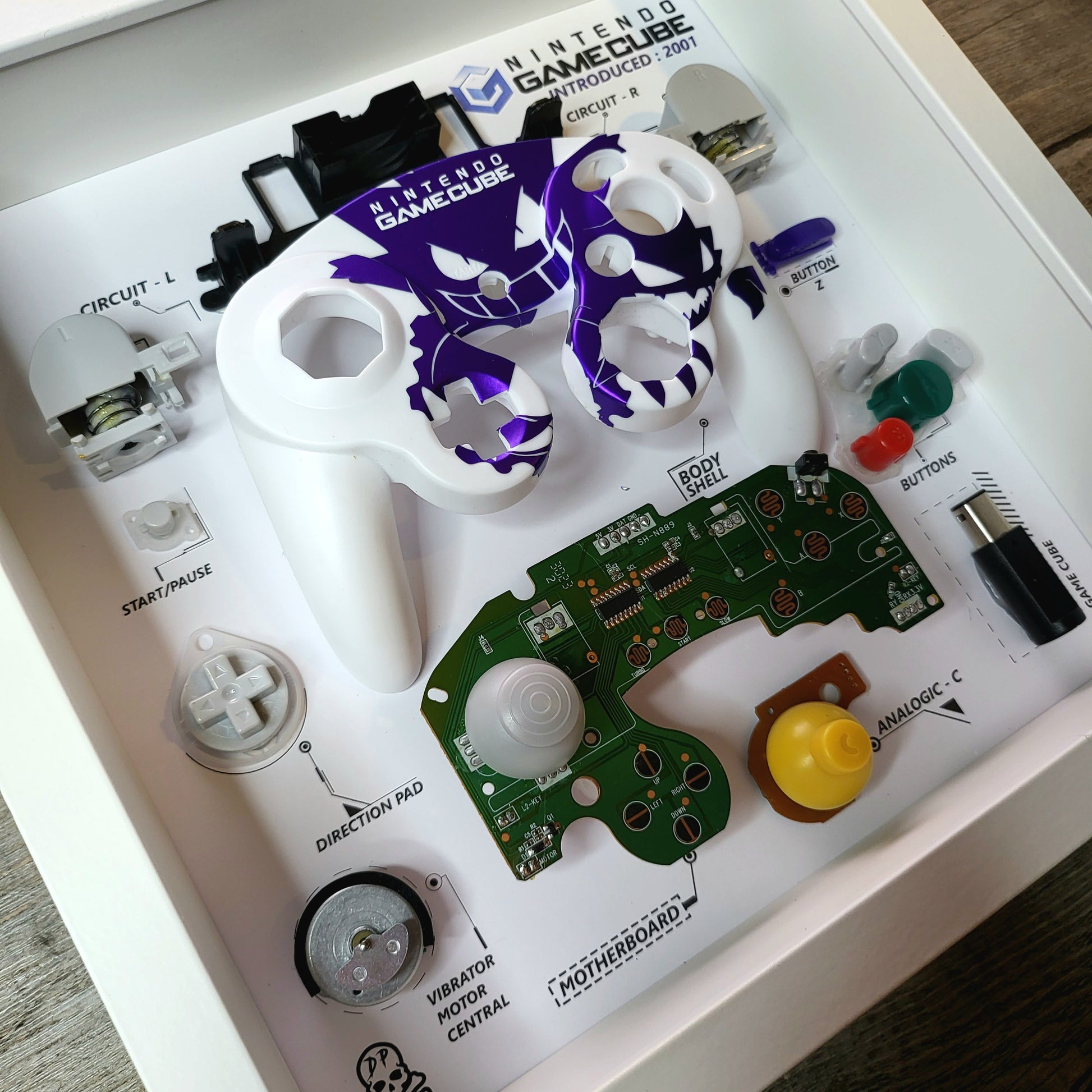 Shadow Box 10x10 with wood frame and polycarbonate glass for wall and Tabletop containing a disassembled controller for Playstation and Nintendo