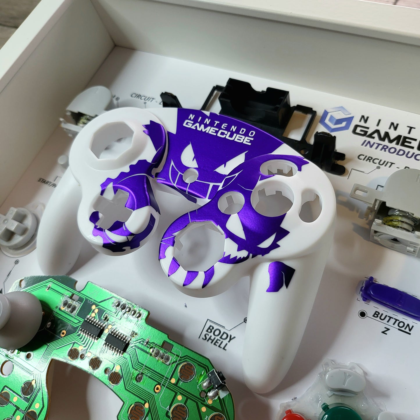 Shadow Box 10x10 with wood frame and polycarbonate glass for wall and Tabletop containing a disassembled controller for Playstation and Nintendo