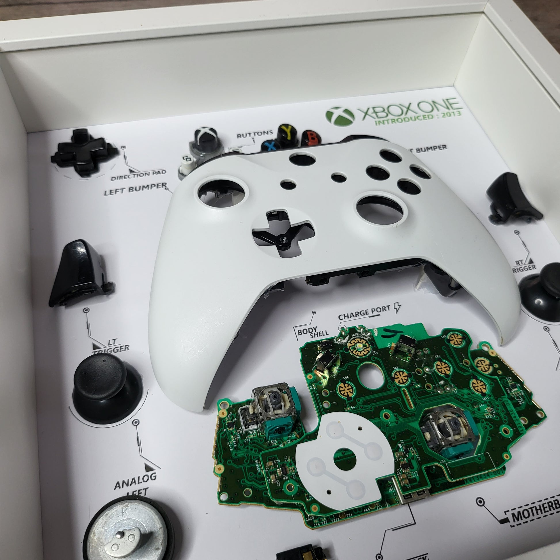 Shadow Box 10x10 with wood frame and polycarbonate glass for wall and Tabletop containing a disassembled controller for Playstation and Nintendo