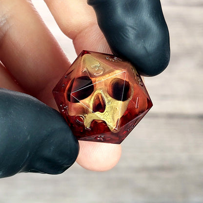 Handmade translucent red resin D20 dice with embedded skull design, held between black-gloved fingers. Gothic tabletop gaming dice with dark fantasy aesthetic for Dungeons & Dragons and RPG players