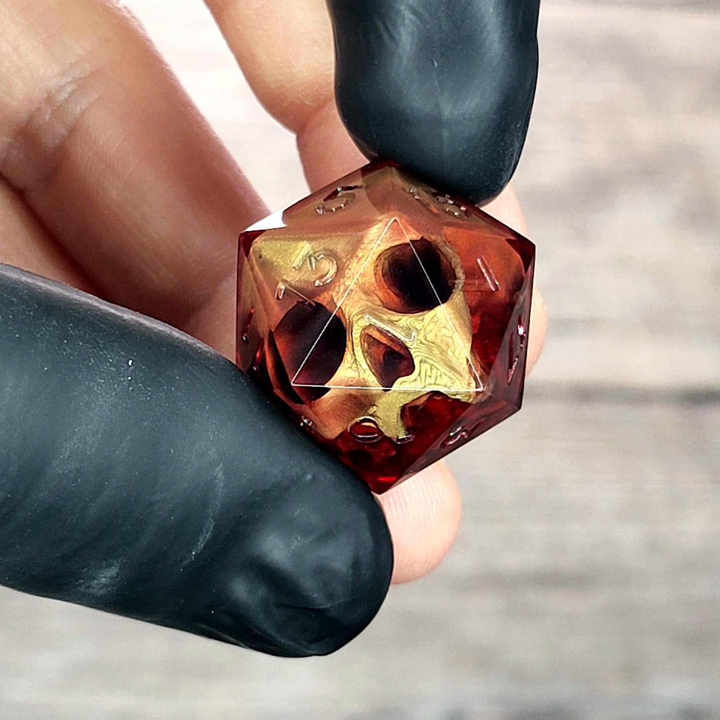 Handmade translucent red resin D20 dice with embedded skull design, held between black-gloved fingers. Gothic tabletop gaming dice with dark fantasy aesthetic for Dungeons & Dragons and RPG players