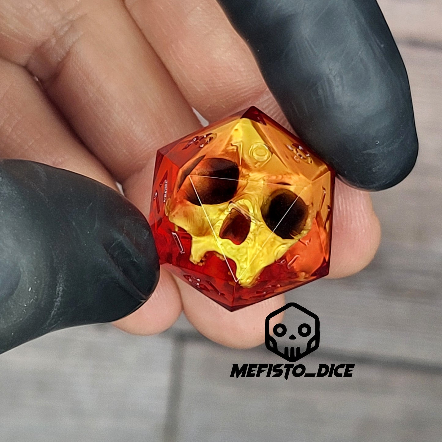 Red translucent resin D20 dice with a gold skull embedded inside, held between black-gloved fingers. Handmade gothic RPG dice for Dungeons & Dragons and dark fantasy tabletop gaming
