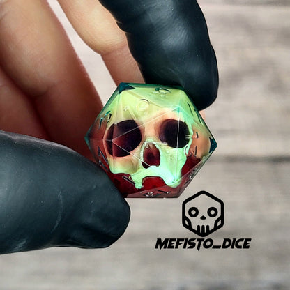 Handmade translucent resin D20 dice with embedded skull design in neon green and deep red colors, held between black-gloved fingers. Unique gothic RPG dice for Dungeons & Dragons and tabletop gaming