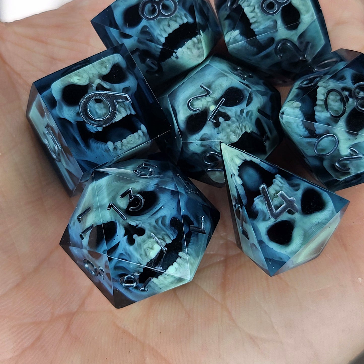 Close-up of black resin dice with mint-green undead zombie skulls and dark metallic silver numbers, handcrafted by Mefisto_Dice.