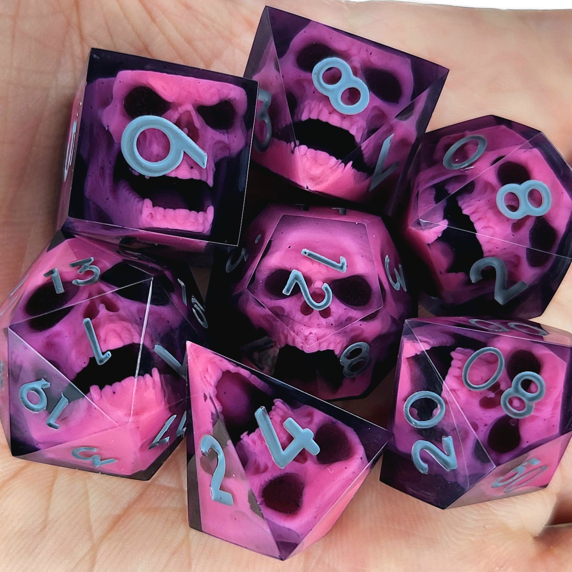 Close-up of black resin dice with pink undead zombie skulls and grey numbers, handcrafted by Mefisto_Dice.