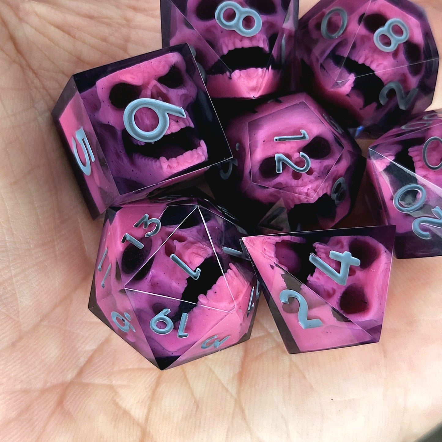 Close-up of black resin dice with pink undead zombie skulls and grey numbers, handcrafted by Mefisto_Dice.